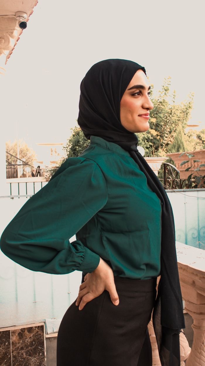 Portrait of a stylish woman in a black hijab and green blouse posing outdoors, exuding confidence.