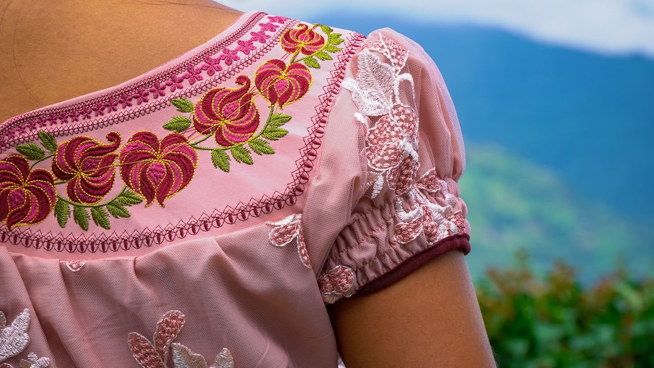 Detailed close-up of an embroidered pink blouse with scenic mountain background in Guatemala.