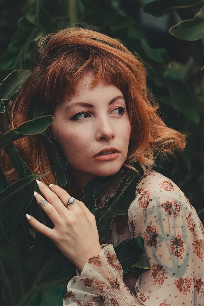 Artistic portrait of a woman with red hair surrounded by lush green leaves.