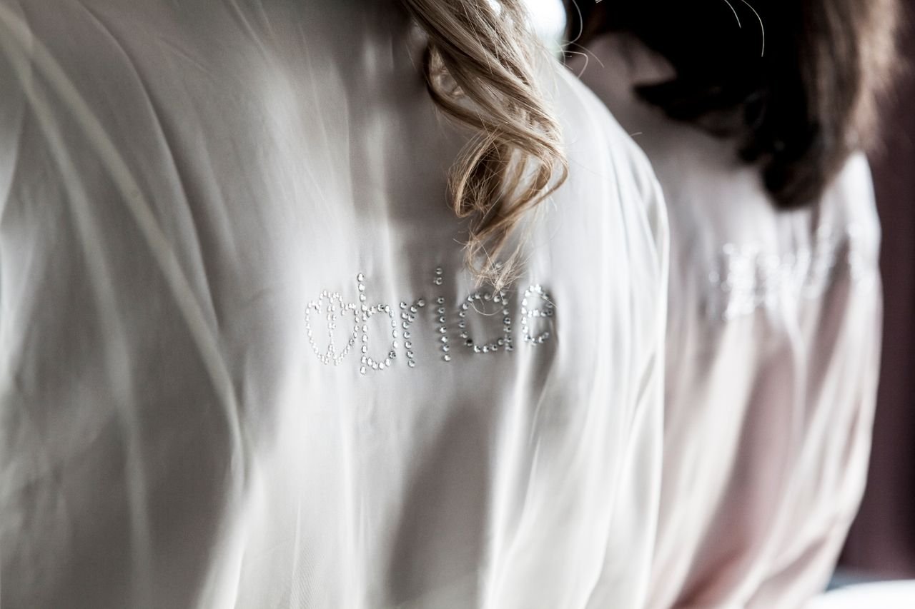Close-up of elegant bride and bridesmaid robes, adorned with beaded text, in soft lighting.