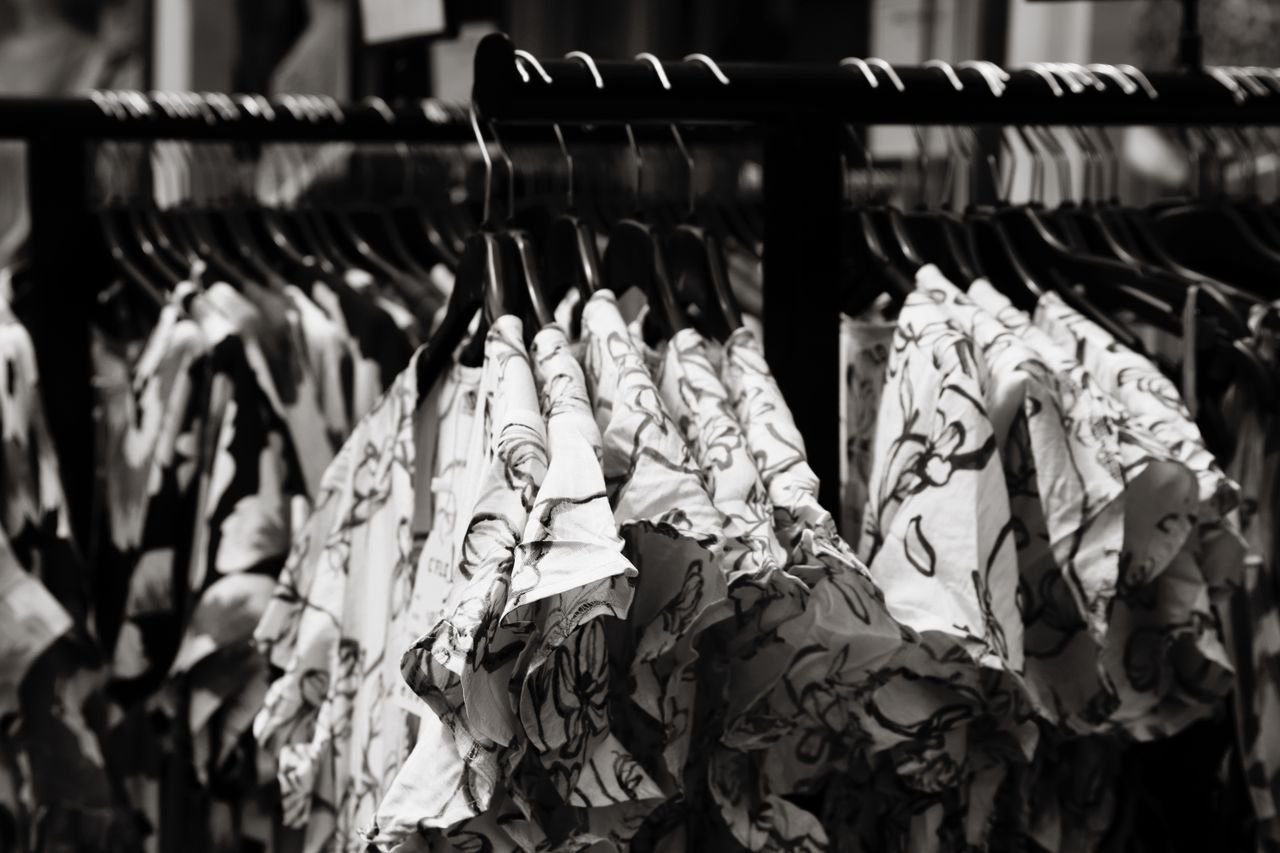 Black and white photo showcasing floral patterned blouses arranged neatly on a clothes rack.