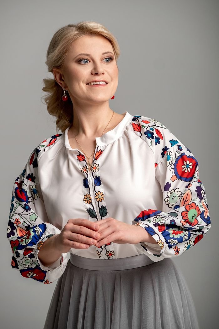 A smiling woman in a floral blouse poses in a studio, exuding elegance and charm.