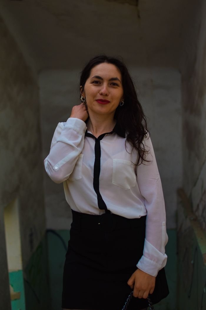 A confident woman poses indoors in a smart casual outfit, exuding elegance and warmth.